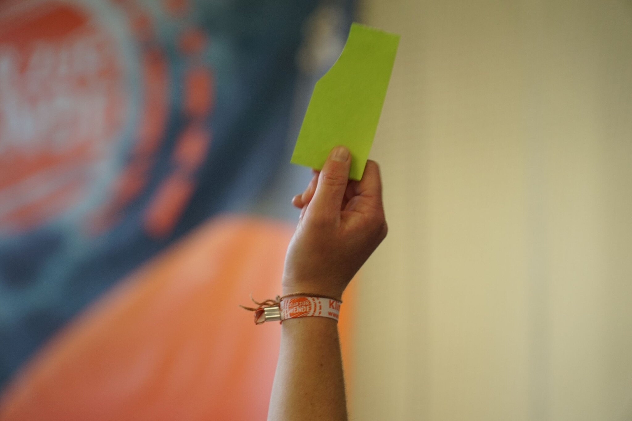 Ein ausgestreckter Arm mit einer Stimmkarte in der Hand vor einem Banner der Jugendklimakonferenz.