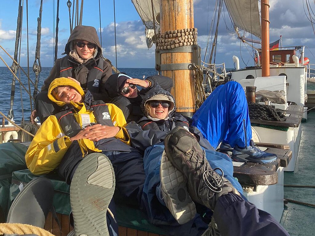 Vier Jugendliche in Segelkleidung sitzen an Bord eines Segelschiffs.