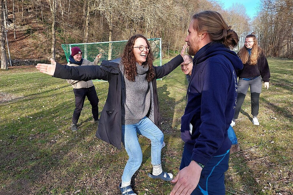 Es sind fünf Menschen zu sehen, die lachen und ein Bewegungsspiel spielen.