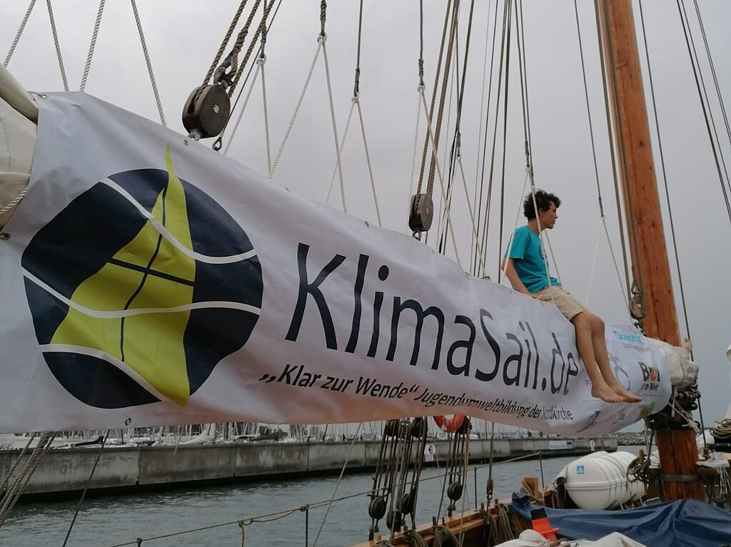Ein langes Banner mit der Aufschrift "KlimaSail" ist über ein gepacktes Segel gespannt.