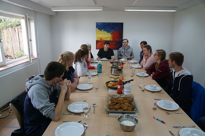 Einige Menschen sitzen an einem langen Tisch, der zum Essen gedeckt ist.