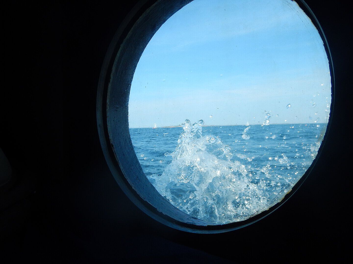Der Blick aus dem Bullauge eines Schiffes, von außen spritzt Wasser ans Glas.ritzt.